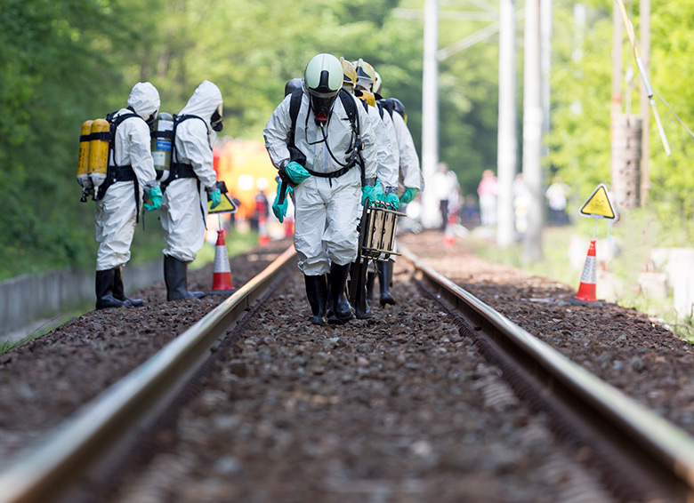 Scientists in protective suits examining a chemical spill near train tracks